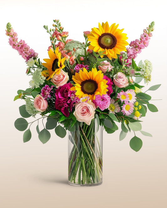 A tall, airy arrangement featuring sunflowers, roses, and textured seasonal flowers. 