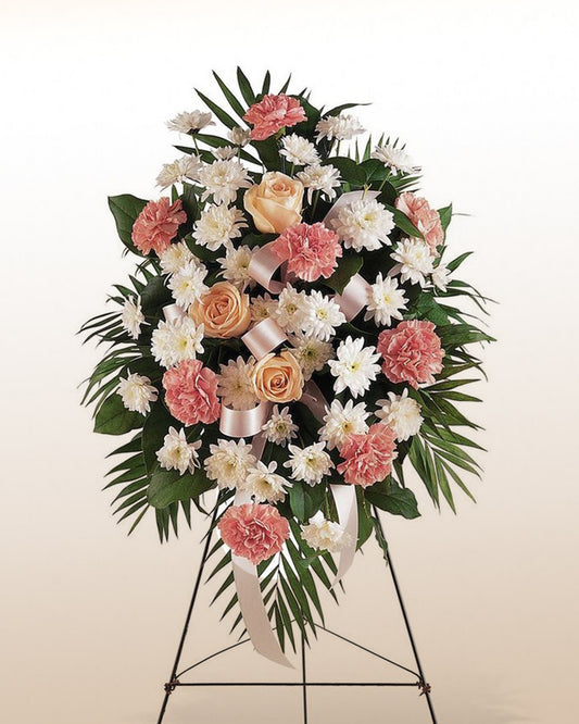 A soft pink and ivory standing floral arrangement with roses and carnations, created to express sympathy with grace and respect.