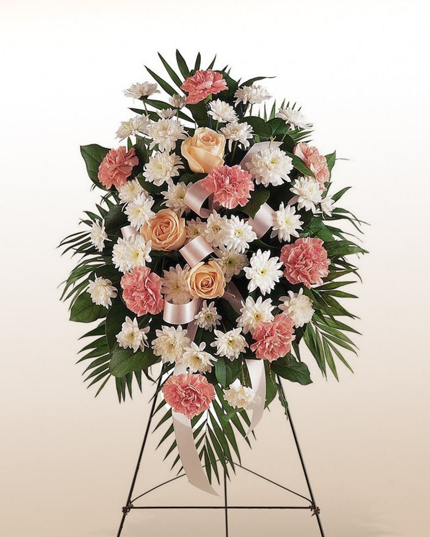 A soft pink and ivory standing floral arrangement with roses and carnations, created to express sympathy with grace and respect.